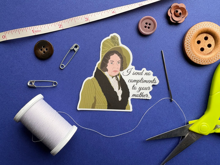 A cartoon of Lady Catherine from Pride and Prejudice 1995 with the text 'I send no compliments to your mother'. Resting on a blue background surrounded by small sewing notions.