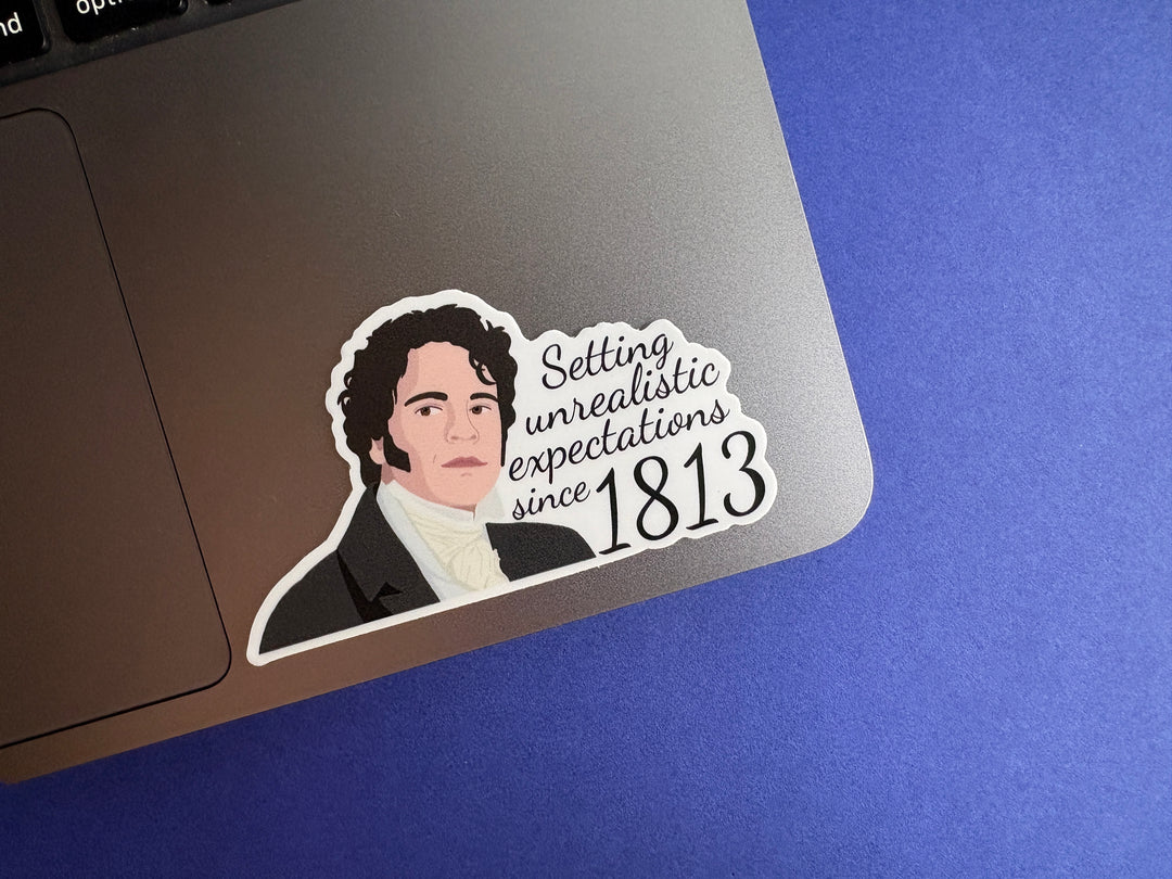 A cartoon of Mr Darcy from Pride and Prejudice with the text 'Setting unrealistic expectations since 1813'. The sticker is resting on a silver laptop on a blue background.