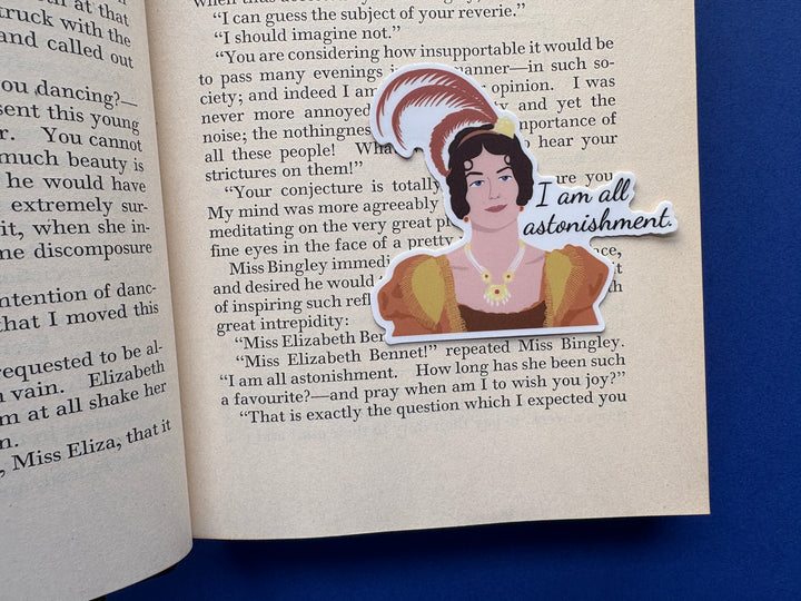 Sticker of a cartoon of Caroline Bingley from Pride and Prejudice 1995 with the text 'I am all astonishment'. Sitting on a book resting on a blue background.