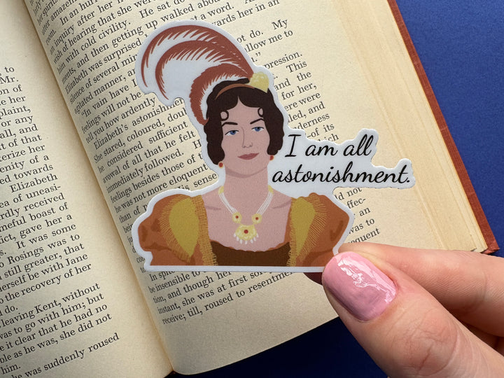 Sticker of a cartoon of Caroline Bingley from Pride and Prejudice 1995 with the text 'I am all astonishment'. Held over a book on a blue background.