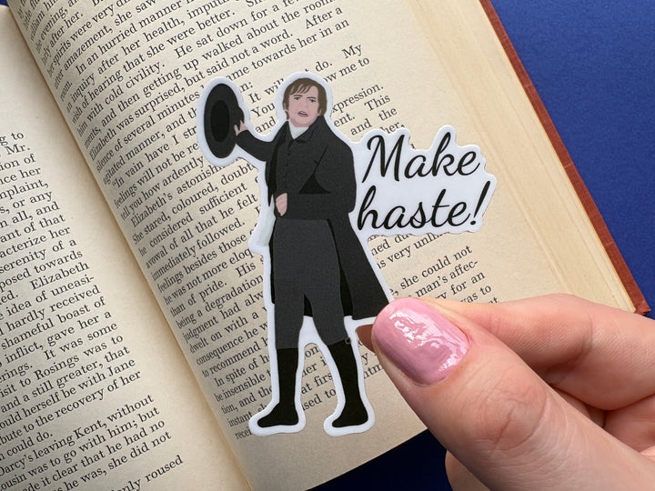 A sticker of Mr Collins from Pride and Prejudice 1995 with the text 'Make haste'. Held above an open book resting on a blue background.