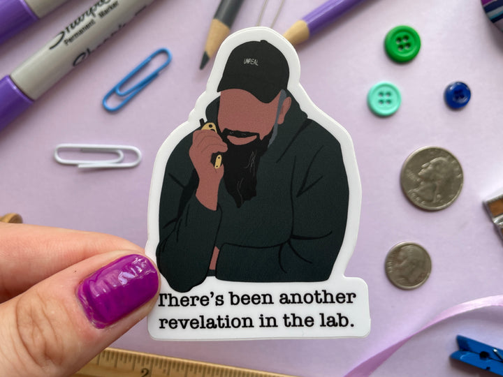 A sticker of a cartoon of comedian Guz Khan holding a walkie talkie with the text "there's been another revelation in the lab" belowis held over a purple background covered in objects.