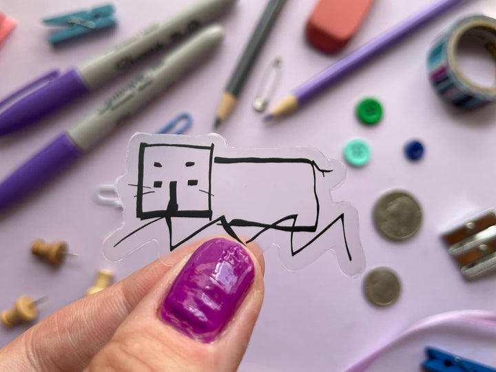 A sticker of a line drawing of a hippo as done by comedian Daisy Mae Cooper on the TV show Taskmaster is held over a purple background covered in objects.