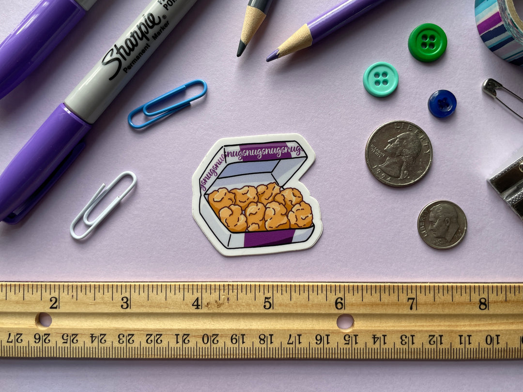 A sticker of a purple and white box of ten chicken nuggets with the word "nugs" repeated along the box is shown on a purple background surrounded by small objects.