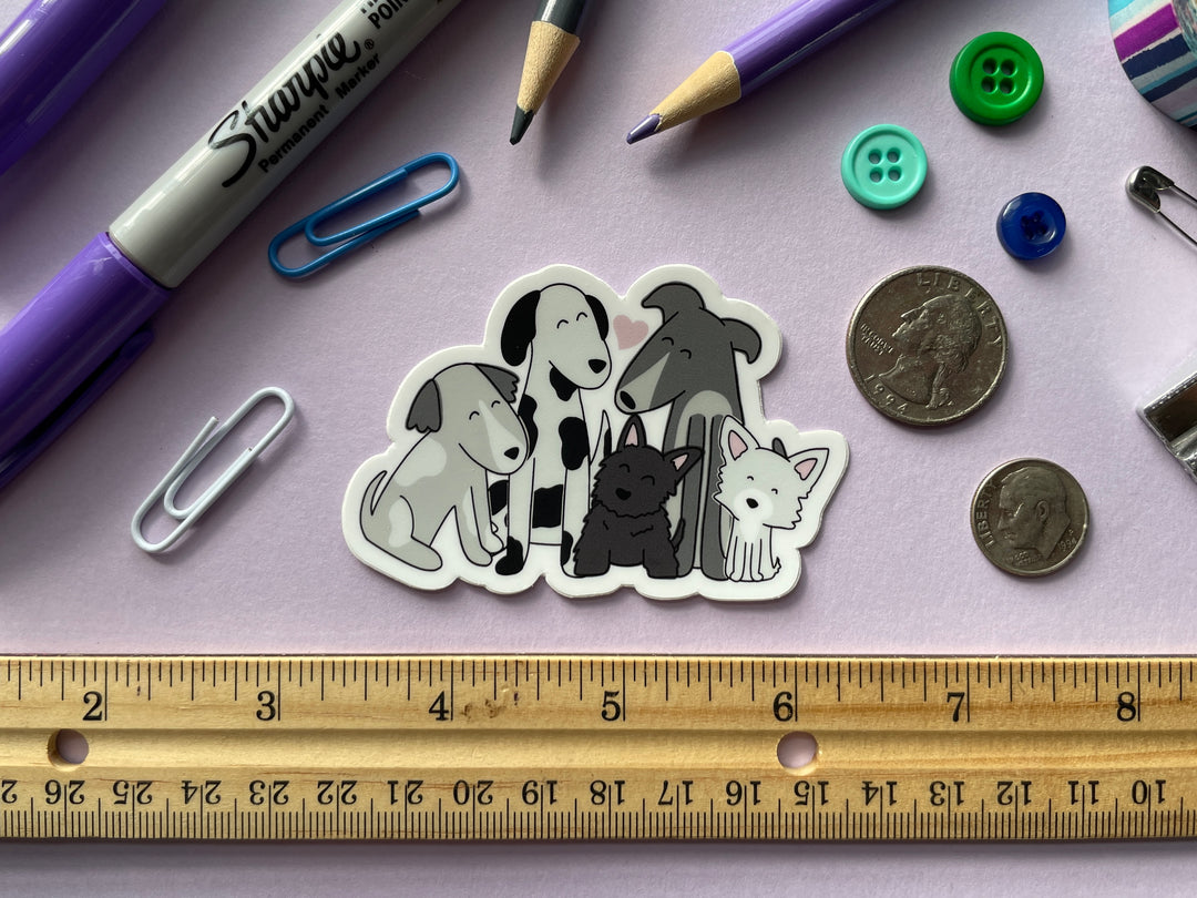 A sticker of a cartoon drawing of five dogs of different sizes in black and white sitting together with a pink heart above them is shown on a purple background surrounded by small objects.