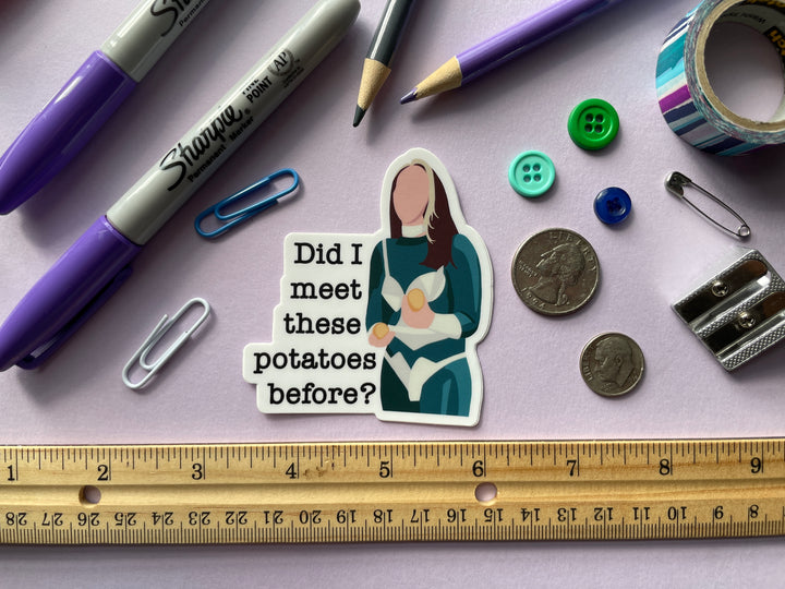 A sticker of a cartoon of comedian Fern Brady holding a potato on the TV show Taskmaster next to the text "Did I meet these potatoes before?" is shown on a purple background surrounded by small objects.