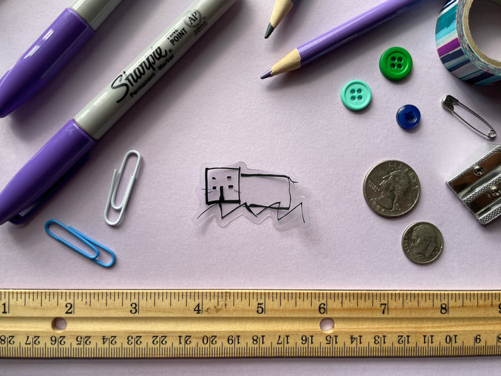 A sticker of a line drawing of a hippo as done by comedian Daisy Mae Cooper on the TV show Taskmaster is shown on a purple background surrounded by small objects.