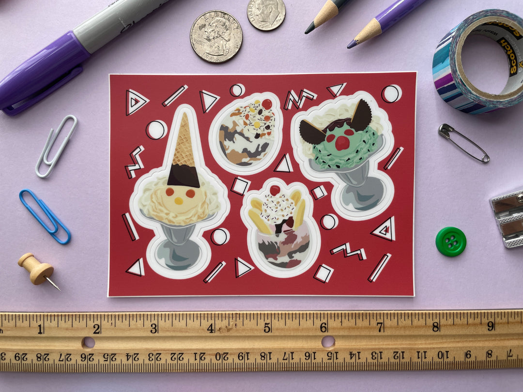 A red sticker sheet with four stickers of cartoon ice cream sundaes, two in silver parfait glasses with faces made from candy and two in glass bowls  is shown on a purple background surrounded by small objects.