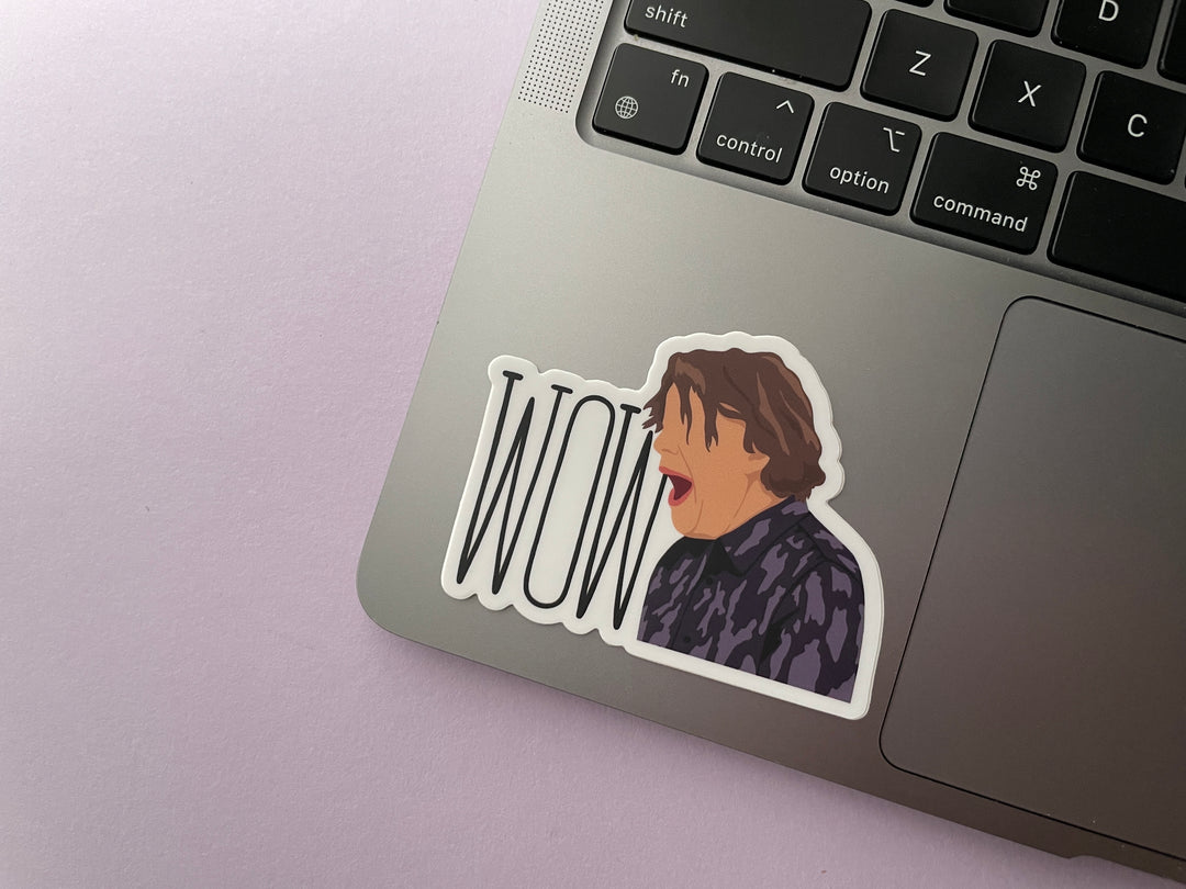 A sticker of a cartoon of comedia Alan Davies with his mouth opening shouting "Wow" from the TV show Taskmaster is shown on a silver laptop.