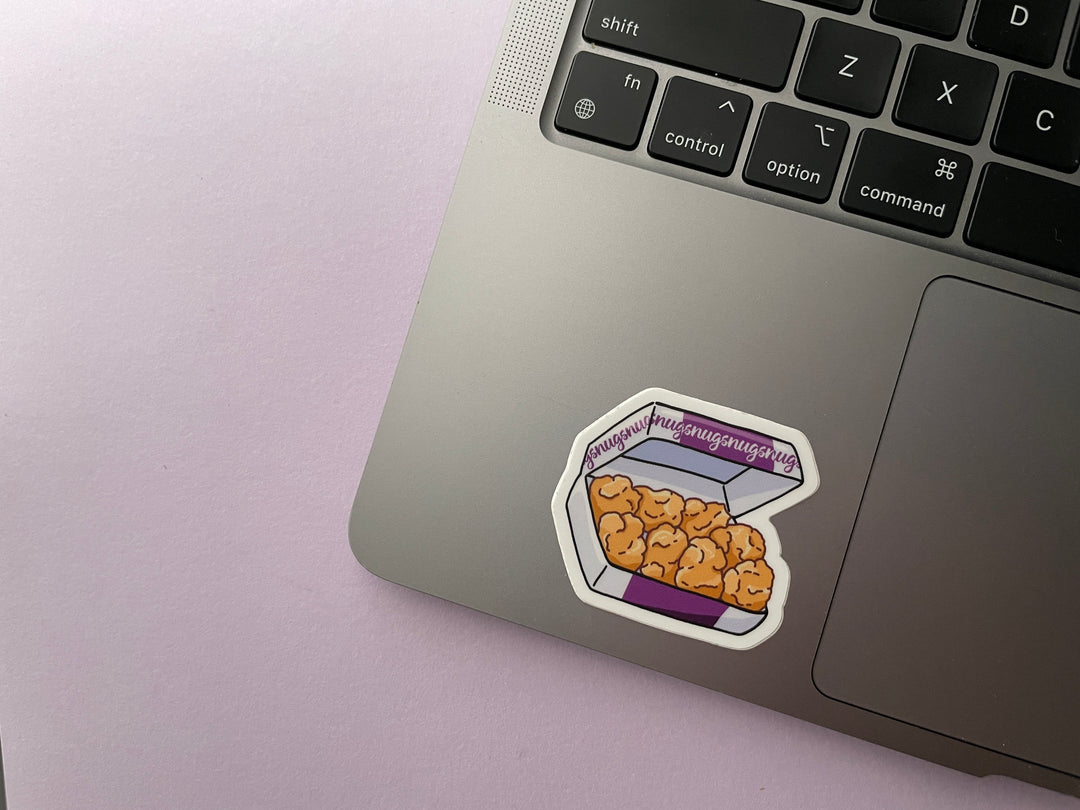 A sticker of a purple and white box of ten chicken nuggets with the word "nugs" repeated along the box is shown on a silver laptop.