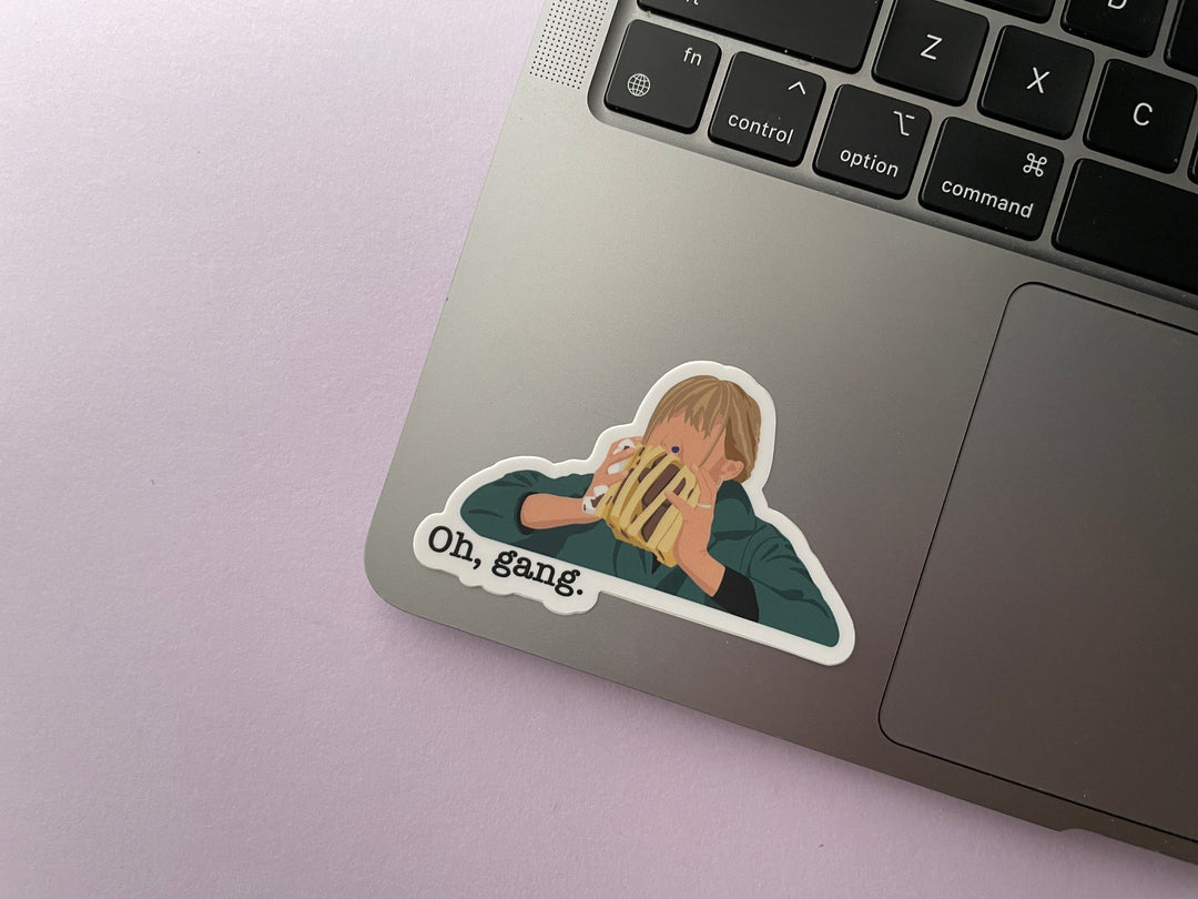 A sticker of a cartoon of comedian Mel Giedroyc eating a sandwich of candy with a blue candy in her nose from the TV show Taskmaster is shown on a silver laptop.