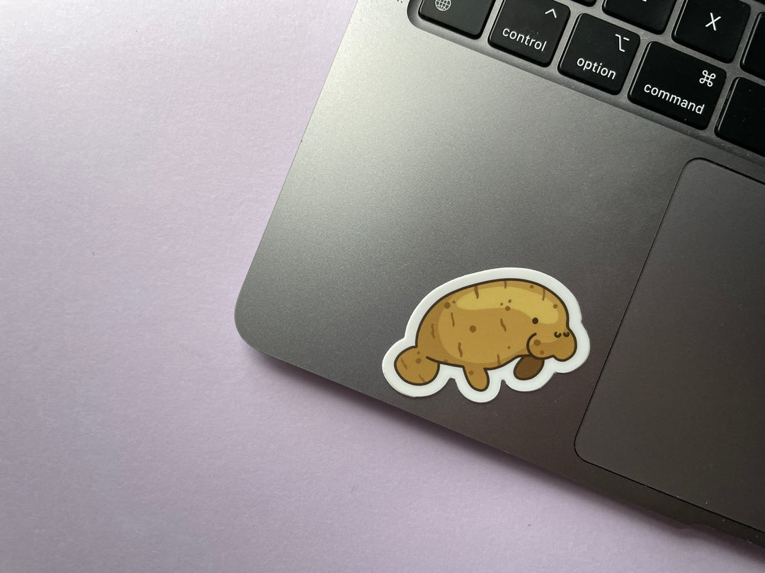 A sticker of a manatee shown in profile colored like a potato is shown on a silver laptop.