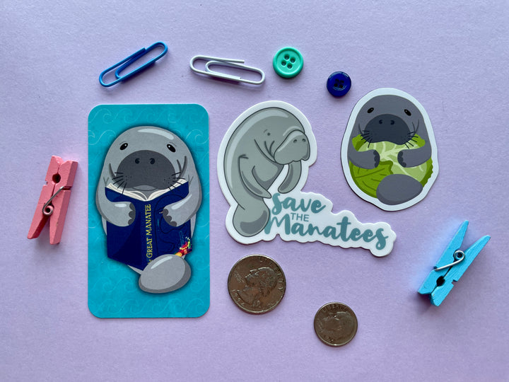 Three items are shown on a purple background surrounded by objects. The items are a manatee bookmark, save the manatees sticker, and manatee hugging lettuce magnet.