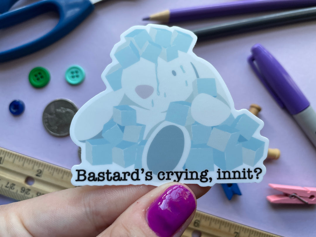 A sticker from the TV show Taskmaster of a stuffed rabbit covered in blue ice cubes and water. Under the rabbit is the text &quot;Bastard&#39;s crying, innit?&quot; The sticker is held over a purple background covered in objects.