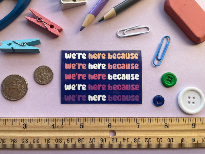 A dark blue sticker with colorful text in bubble letters reads "we're here because" repeating five times. The sticker is on a purple background covered in objects.