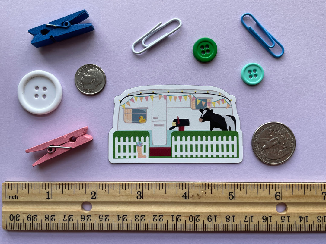 A magent of the caravan from the TV show Taskmaster with a cow in the front yard and duck in the window is shown on a purple background surrounded by objects.